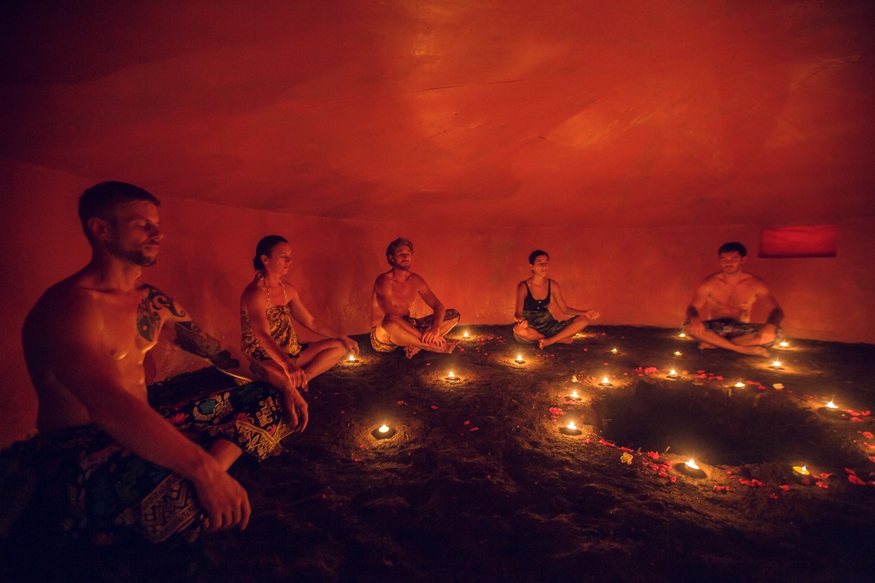 Group of people inside Mayan Temazcal- traditional steam sauna bath of Mesoamerican cultures. Diverse multiethnic people sitting around candle lights in circle in darkness and meditating
